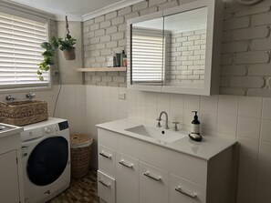 A modern bathroom with a brick wall, a large mirror, a sink, and a washing machine. - location location 5min walk to beach, lake, restaurants and shops (Merimbula)