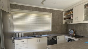 Une cuisine moderne avec des meubles blancs, un réfrigérateur en acier inoxydable, un lave-vaisselle et une fenêtre équipée de stores.
