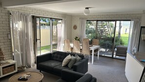 Un salon avec un canapé gris foncé, une table basse ronde et un coin repas avec des chaises en osier.