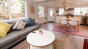 Ein modernes Wohnzimmer mit einem grauen Sofa, einem weißen Couchtisch und einem Essbereich mit einem roten Teppich mit Muster.