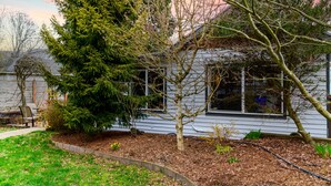 Ein Haus mit einem gepflegten Garten, einem großen immergrünen Baum und einem kleinen Baum vor der Fassade.