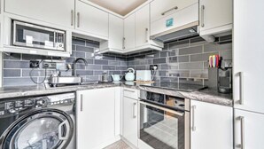 A compact kitchen with white cabinets, a built-in microwave, a washing machine, and a dishwasher. - Torpoint - Apartment - Sleeps4 - Seaside - Parking (Torpoint)