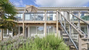 A beachfront property with a glass-enclosed balcony, outdoor seating, and a staircase leading to a deck. - Torpoint - Apartment - Sleeps4 - Seaside - Parking (Torpoint)