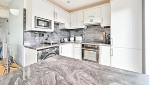 A modern kitchen with white cabinets, a microwave, a stove, and a dishwasher. - Torpoint - Apartment - Sleeps4 - Seaside - Parking (Torpoint)