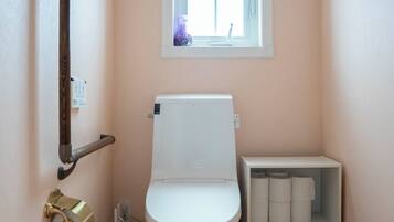A small bathroom with a toilet, a shelf with toilet paper, and a window above the toilet.