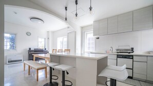 A modern kitchen with white cabinetry, a central island with bar stools, and a dining area with wooden chairs and a bench. - THE GARNET HIGASHIKAWA (Higashikawa)