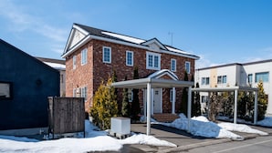 A two-story brick house with a covered porch and a snow-covered driveway. - THE GARNET HIGASHIKAWA (Higashikawa)