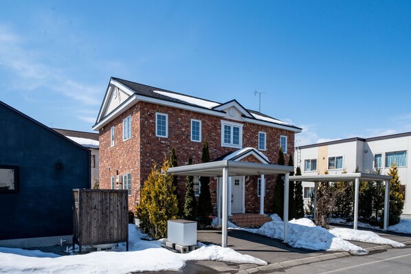 A two-story brick house with a covered porch and a snow-covered driveway. - THE GARNET HIGASHIKAWA (Higashikawa)