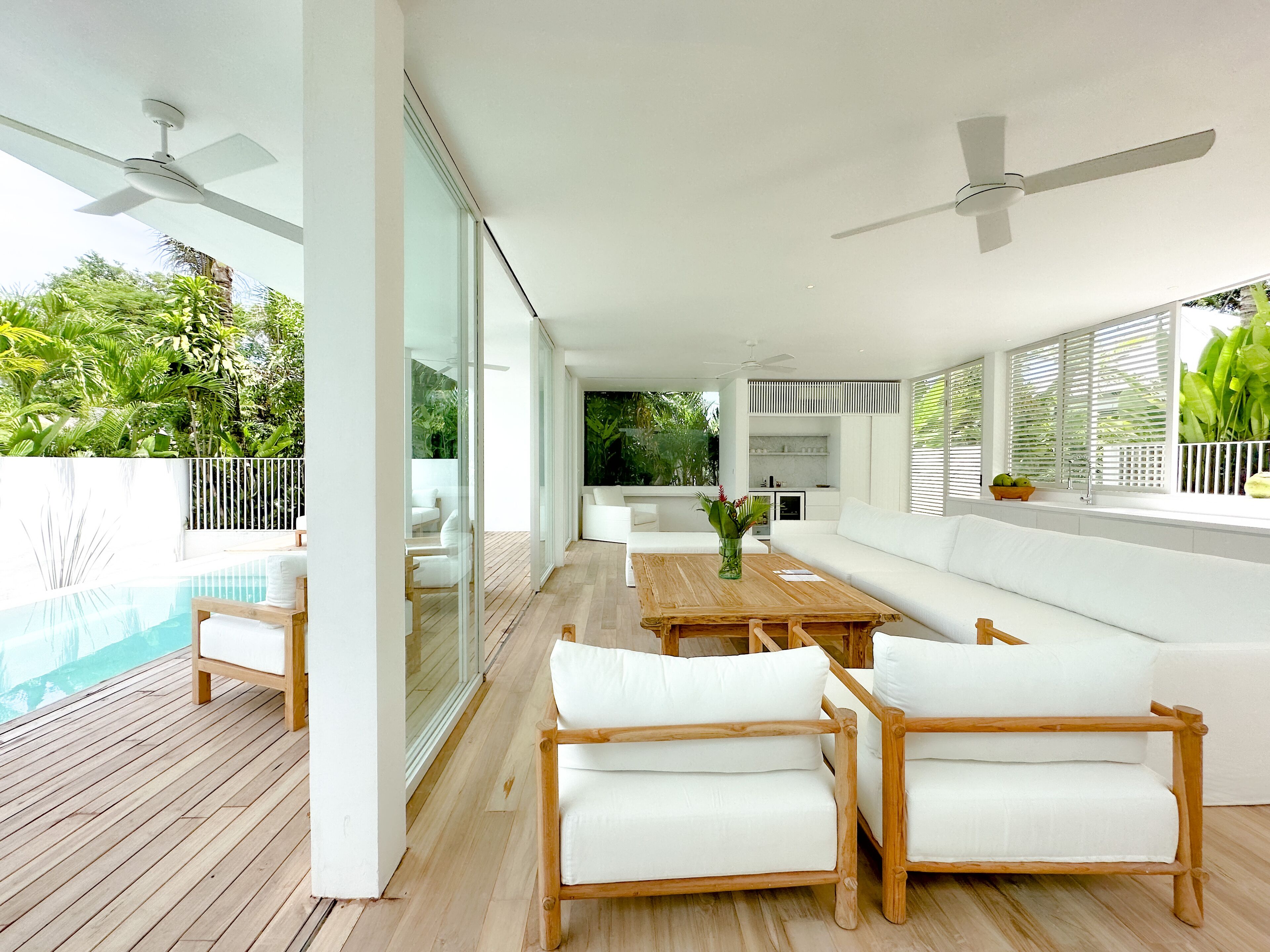 A modern outdoor living area with a pool, white furniture, and a view of lush greenery.