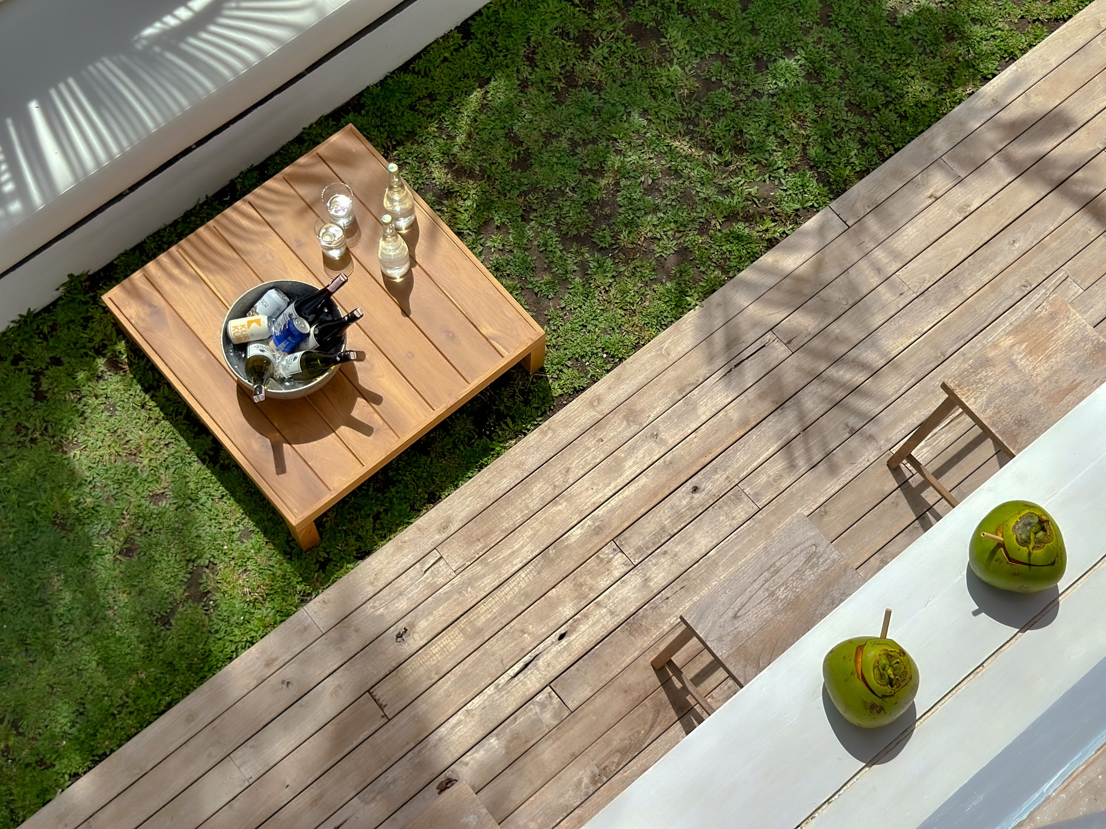 A wooden deck with a table set for two, a bucket of bottles, and two green fruits.