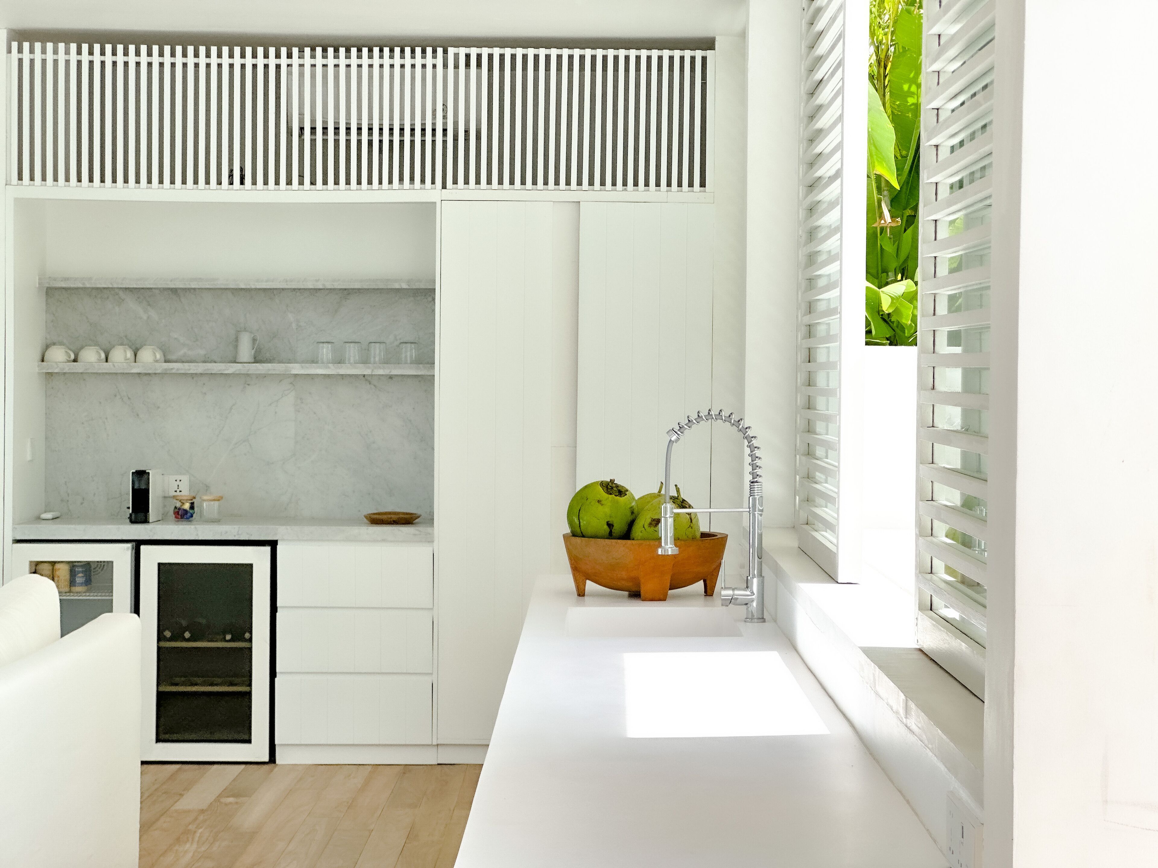 Una cocina moderna con armarios blancos, encimera de mármol y un cuenco de madera con frutas.