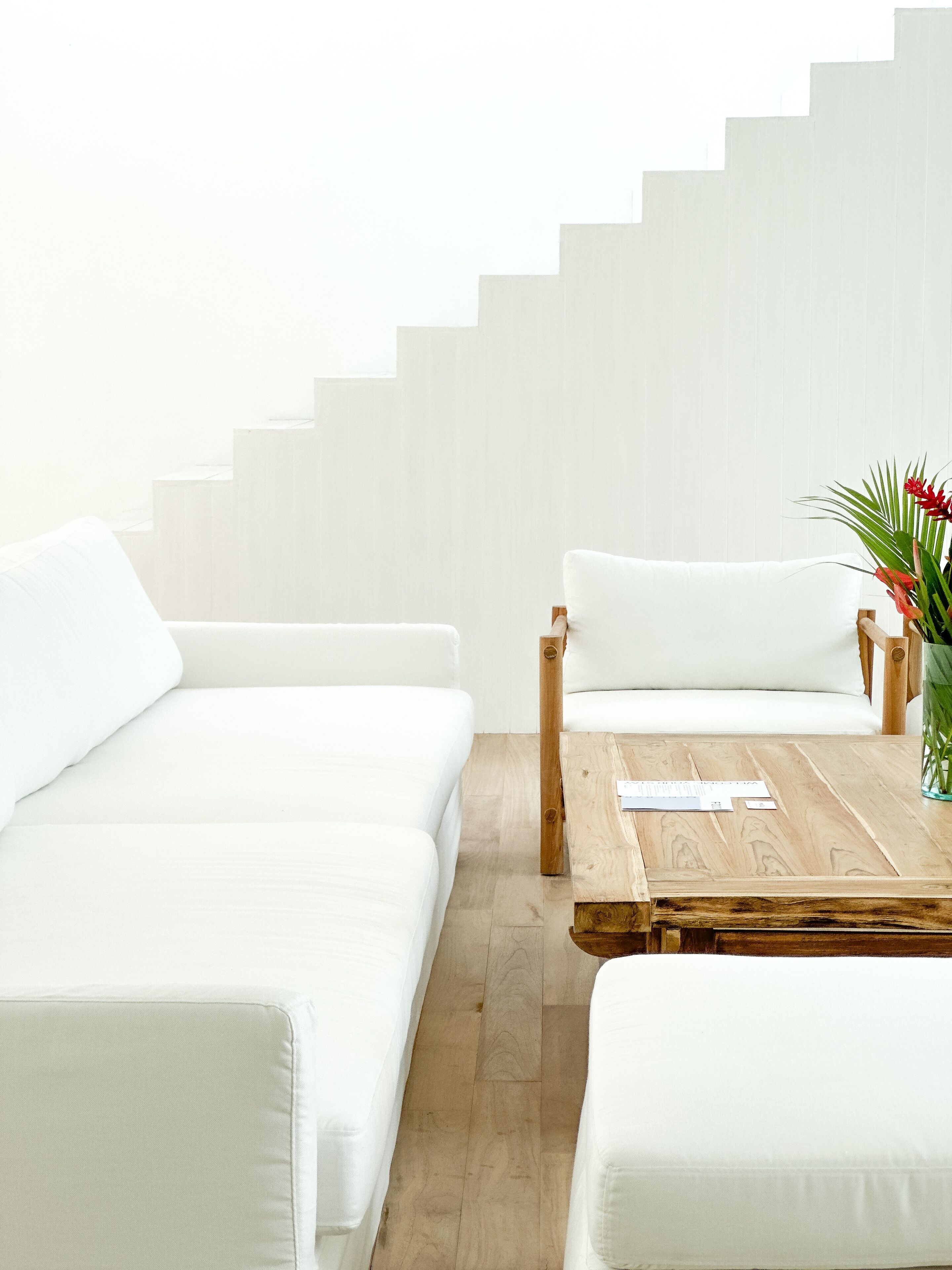 A modern living room with a white sofa, a wooden coffee table, and a staircase in the background.