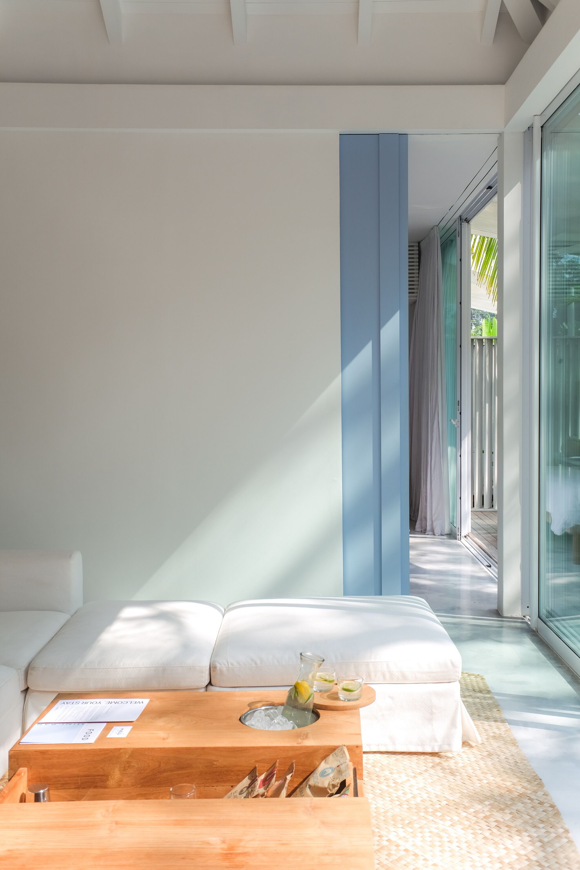 Une pièce moderne avec un canapé blanc, une table basse en bois et une porte vitrée donnant sur un balcon.