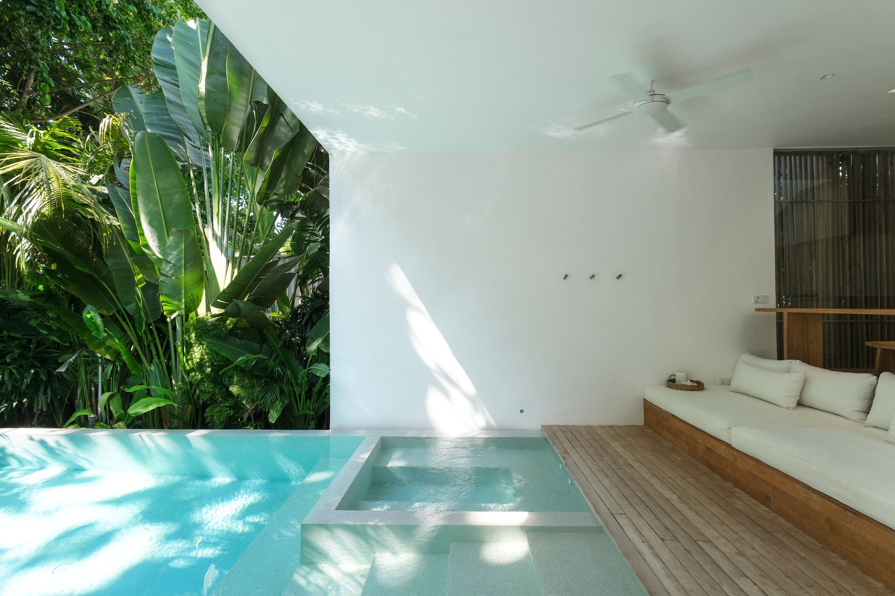 A modern room with a pool, a ceiling fan, and a white sofa.