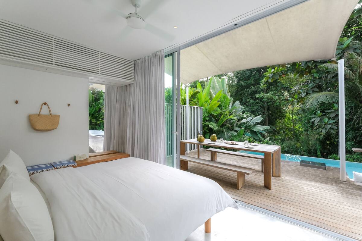 Une chambre avec un grand lit, un banc en bois et une vue sur une végétation luxuriante.