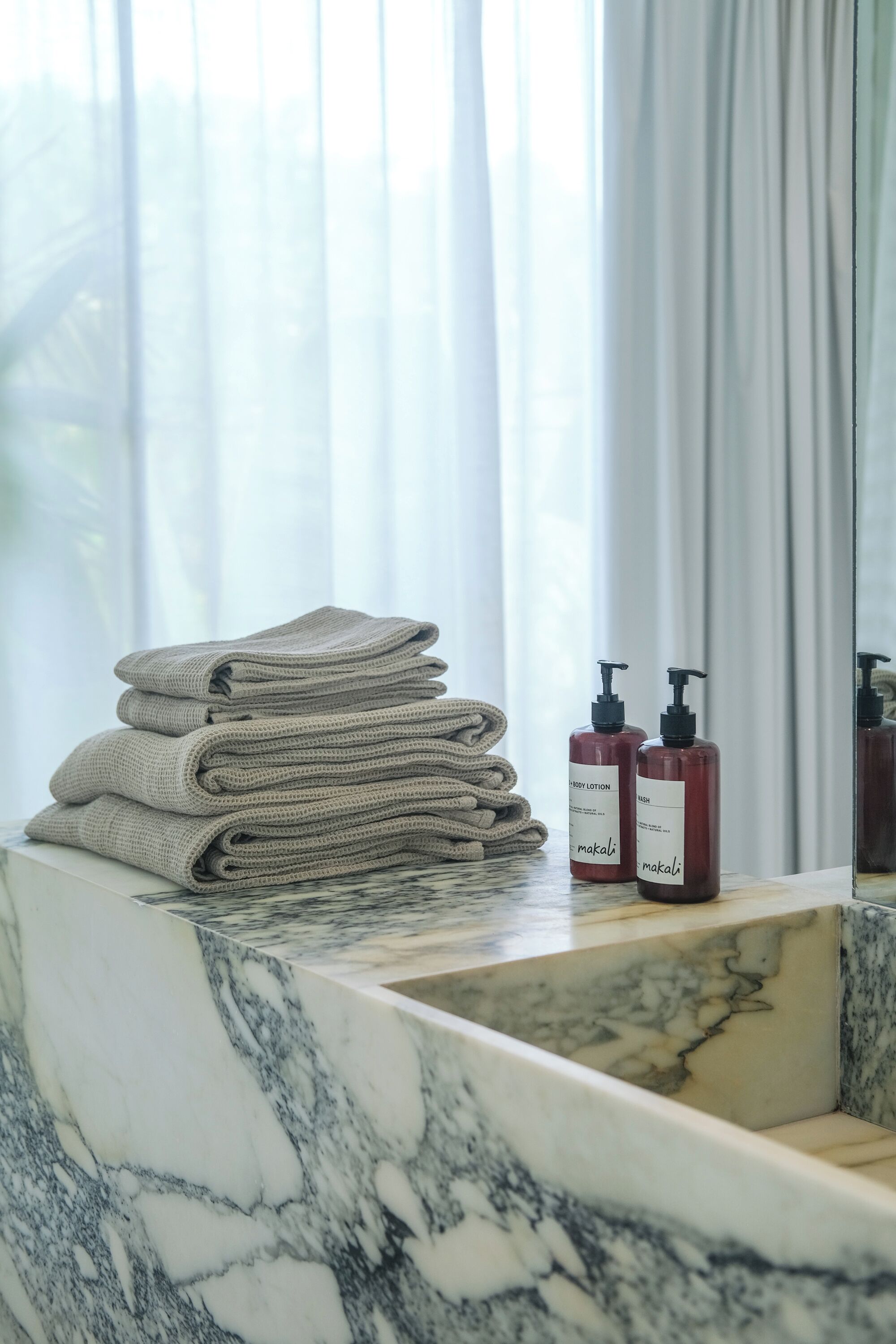 A bathroom with a marble sink, a stack of folded towels, and two bottles of lotion.