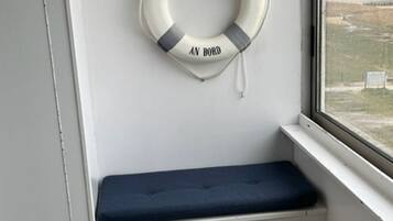 Ein Fensterplatz mit dunklem Kissen und einem Rettungsring an der Wand.