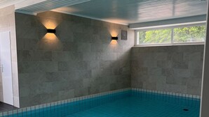 An indoor swimming pool with tiled walls and ceiling, and two wall-mounted light fixtures. - Ferienwohnung mit Maritimer Ausstattung, Seeblick und Schwimmbad - Haus Seehund (Cuxhaven)