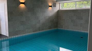 Ein Innenpool mit gefliesten Wänden und Decke sowie zwei Wandleuchten.
