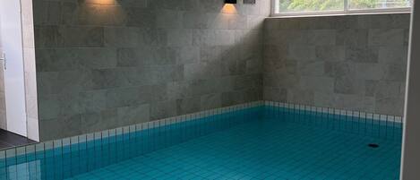 An indoor swimming pool with tiled walls and ceiling, and two wall-mounted light fixtures.