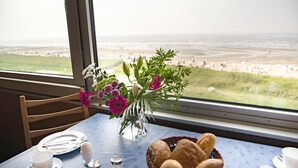 A dining table with a view of the beach, a vase with flowers, and a basket of bread. - Ferienwohnung mit Maritimer Ausstattung, Seeblick und Schwimmbad - Haus Seehund (Cuxhaven)