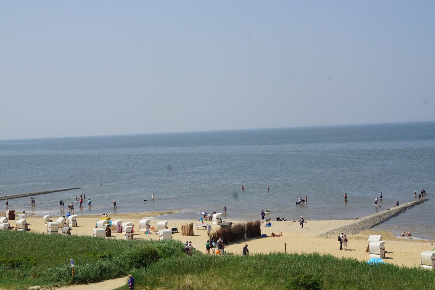 Ein Strand mit Menschen, einem Steg und Liegestühlen.