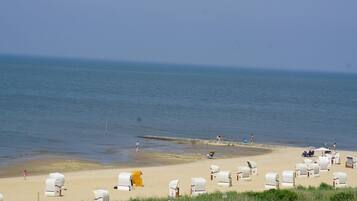 Ein Strand mit mehreren Reihen von Sonnenschirmen und ein paar Personen im Wasser.