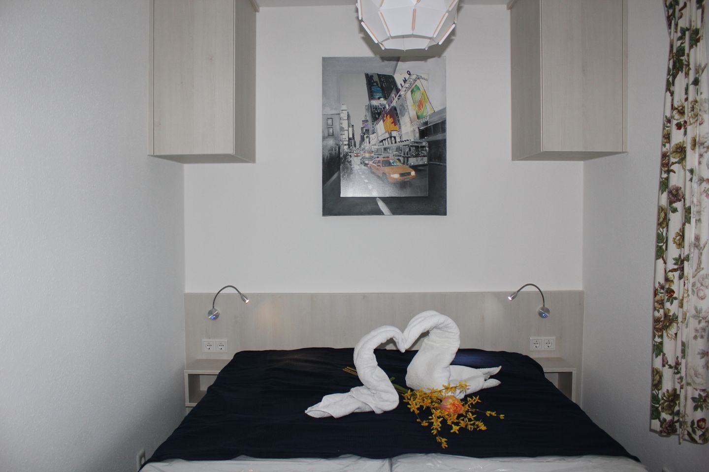 Ein Hotelzimmer mit Bett, Wandbild, Leuchte und einem blumigen Vorhang.