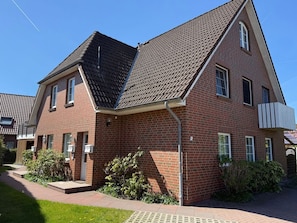 Ein zweistöckiges Backsteinhhaus mit einem steilen Dach, einem sichtbaren Schornstein und einer kleinen Veranda.