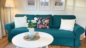Ein blaugrünes Sofa mit weißen und floralen Kissen, ein weißer Couchtisch mit Kerzen und gerahmte Bilder an der Wand.