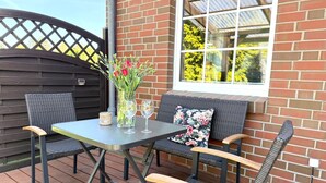 A patio with a table and chairs, a vase with flowers, and a window with a view of greenery.