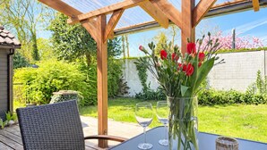 A covered outdoor patio with a table, chairs, and a vase of flowers.