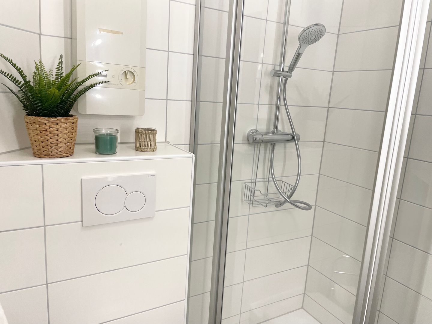 Ein Badezimmer mit Duschkabine aus Glas, einem Blumentopf, einem an der Wand befestigten Lichtschalter und einem kleinen Regal mit Dekoration.