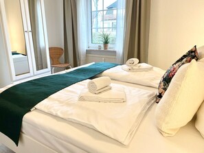 Een hotelkamer met twee bedden, een raam met gordijnen, een stoel en een kleintje tafeltje met een plant.