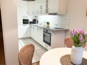 Une cuisine moderne avec des meubles blancs, un four à micro-ondes, une machine à café et un four. On y trouve une table à manger avec des chaises et un vase rempli de fleurs.