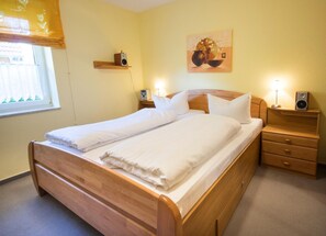 Un lit double bien fait, avec une tête de lit en bois, des tables de chevet équipées de haut-parleurs et une étagère fixée au mur.