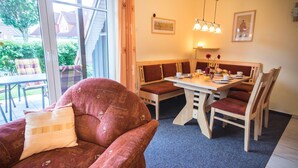 A cozy room with a large window, a dining table with chairs, and a sofa with a cushion.