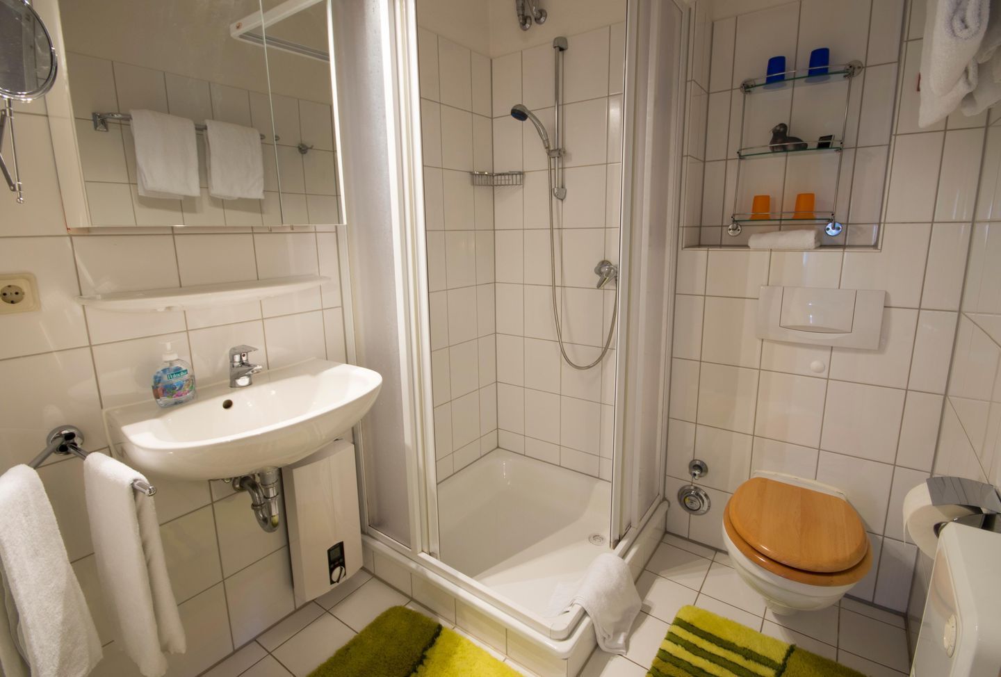 Ein Badezimmer mit Waschbecken, Spiegel, Dusche, Toilette und einem kleinen Ablagefach für Toilettenartikel.