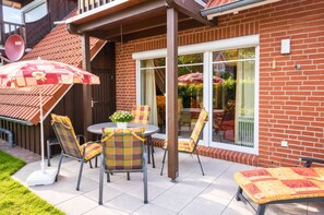 Une terrasse avec une table et des chaises, un pot de fleurs et un parasol rouge.