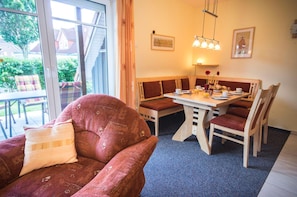 Une pièce confortable avec une grande fenêtre, une table à manger avec des chaises et un canapé agrémenté d’un coussin.