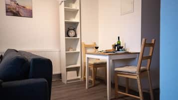 A room with a white wall, a clock, a small table with chairs, a radiator, and a picture of a beach.
