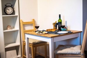 Una mesa de comedor con una botella de vino, copas, pan y aceitunas.