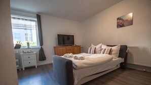 A bedroom with a bed, a TV, a dresser, and a window with curtains.