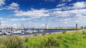 Ein Hafen mit mehreren Segelbooten, einem Leuchtturm und Industriegebäuden im Hintergrund.