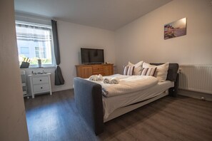 Un dormitorio con cama, televisor, cómoda y ventana con cortinas.
