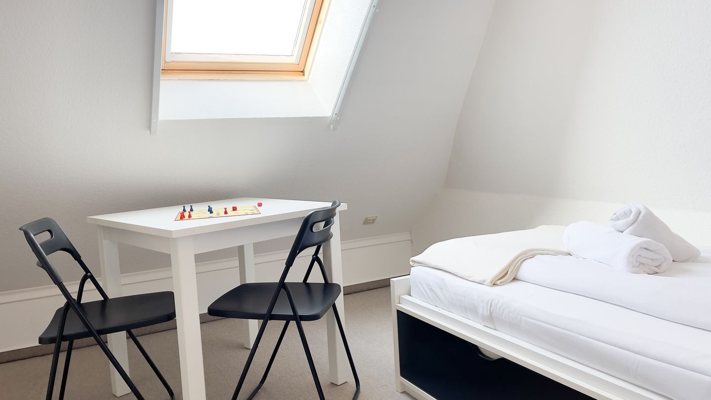 Een slaapkamer met een bed, een wit bureau, twee stoelen en een dakraam.