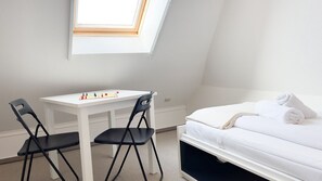 Un dormitorio con una cama, un escritorio blanco, dos sillas y un tragaluz.