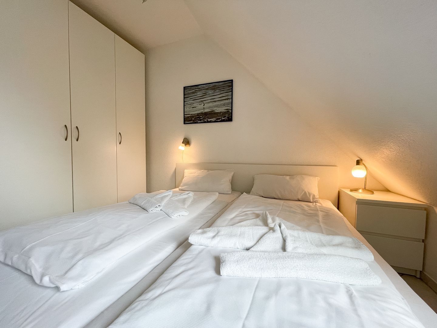 A bedroom with a bed, two bedside tables, a nightstand, and a wardrobe.