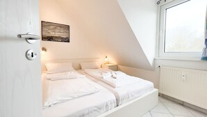 A bedroom with two beds, a window, a radiator, and a door with a keyhole. - Hamburger Straße 28 - Apartment Jonathan in the spa town of Sahlenburg (Cuxhaven)