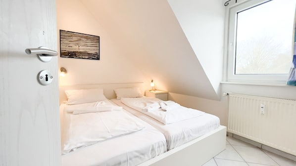 A bedroom with two beds, a window, a radiator, and a door with a keyhole.